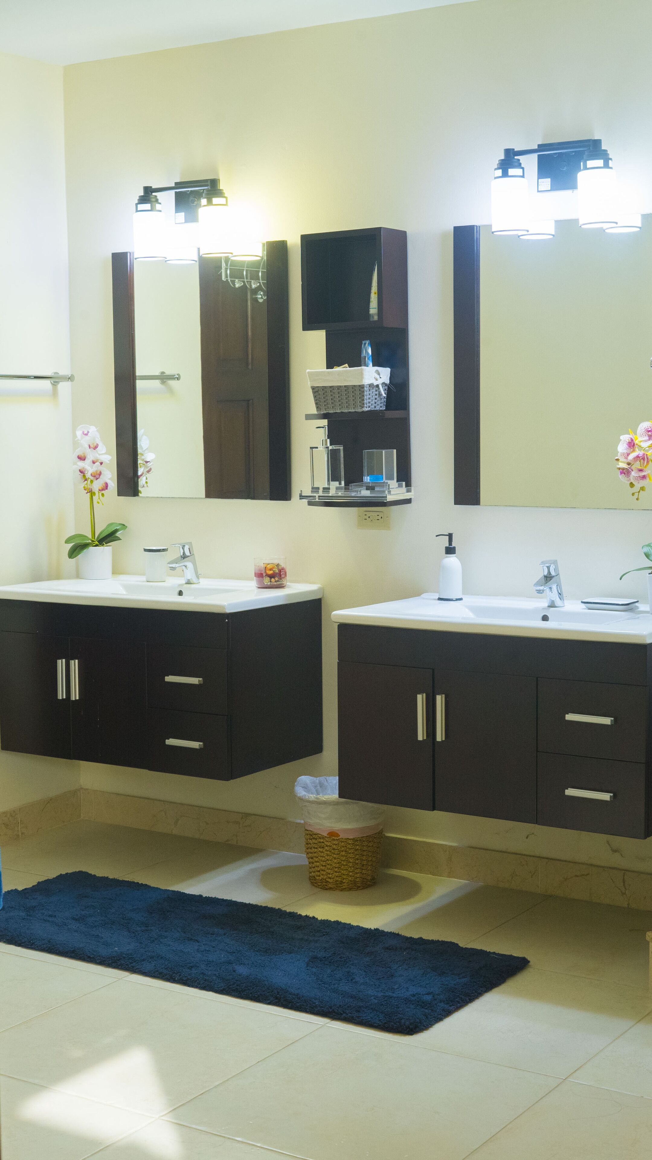 A bathroom with two sinks, dark cabinets, a mirror, and a blue rug.