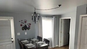 Un comedor con una mesa de madera dispuesta para cuatro, una araña y un arreglo floral colgando en la pared.