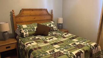 A bed with a wooden headboard, a quilt with animal patterns, two bedside lamps, and a nightstand with a lamp.