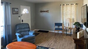 Una sala de estar con un sillón azul, una mesa de centro de madera y una mesita auxiliar con una lámpara y una planta.
