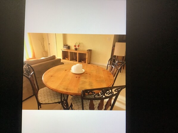 A round wooden dining table with a white hat on it, surrounded by four chairs with intricate metal designs.