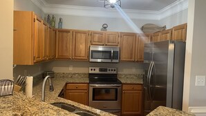 A kitchen with wooden cabinets, stainless steel appliances, granite countertops, and a ceiling light fixture.