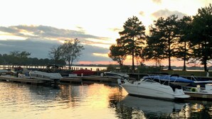 A marina with boats docked, calm water, and trees in the background.