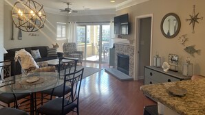 A spacious living room with a glass dining table, a fireplace, and a balcony with sliding doors.