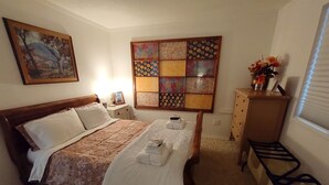 Ein ordentlich eingerichtetes Schlafzimmer mit einem großen Bett, einem Nachttisch mit Lampe, einer Kommode und einem Fenster mit Jalousien.