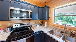 Une cuisine moderne avec des meubles de couleur bleu foncé, des appareils électroménagers en acier inoxydable, des comptoirs en granit et une fenêtre donnant sur un paysage verdoyant.