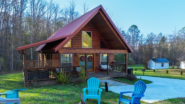 Une cabane en rondins avec un porche, un foyer et des chaises Adirondack bleues.