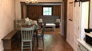 Un intérieur rustique avec des poutres apparentes, un coin repas comprenant une table et des chaises, un canapé et un espace cuisine avec des placards.