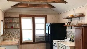 Une cuisine avec des poutres en bois, des meubles blancs, un réfrigérateur noir et une fenêtre donnant sur un paysage agréable.