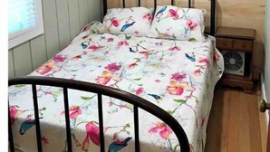 Un lit simple avec une couvre-lit à motifs floraux, dans une pièce aux murs en bois et dotée d’une fenêtre.
