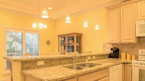 Una cocina con encimeras de granito, fregaderos de acero inoxidable, armarios de madera e iluminación colgante.