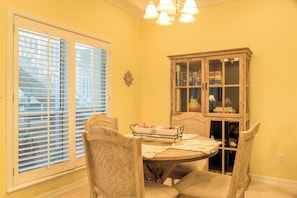 A dining room with a round table, four chairs, a cabinet with glass doors, and a window with blinds.