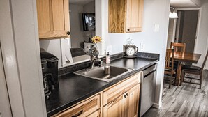 A kitchen with wooden cabinets, a black countertop, a sink, a coffee maker, and a clock.