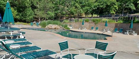 A pool area with green lounge chairs and tables, surrounded by trees.