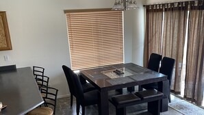 A dining area with a large table, chairs, and a bench. There is a window with blinds, a ceiling light, and a rug on the floor. - Great home in fantastic location! Close to everything! Heated pool! (Chandler)