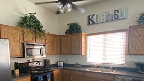 A kitchen with wooden cabinets, a microwave, a stove, a ceiling fan, and a window with blinds. - Great home in fantastic location! Close to everything! Heated pool! (Chandler)