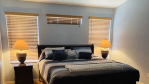 A bedroom with a bed, two bedside tables with lamps, a wooden floor, and a gray rug. - Great home in fantastic location! Close to everything! Heated pool! (Chandler)