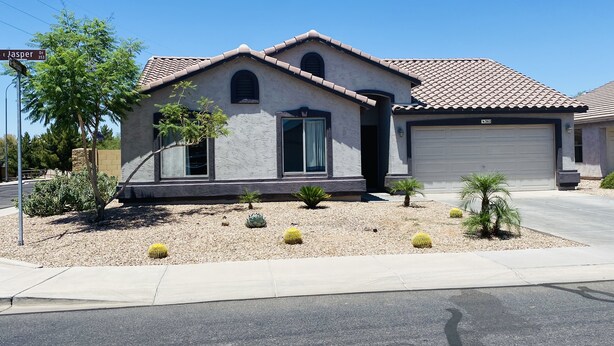 A single-story house with a tiled roof, a garage, and a landscaped front yard with cacti and small trees. - Great home in fantastic location! Close to everything! Heated pool! (Chandler)