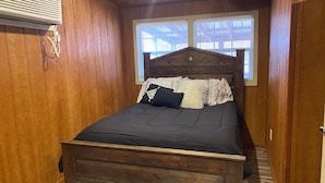 Quarto com painéis de madeira, uma cama, uma janela e ar condicionado fixado na parede.