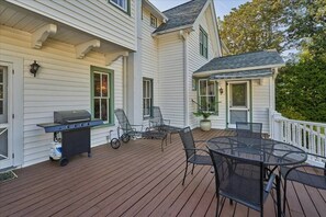 Een houten terras met een barbecue, stoelen en een tafel.