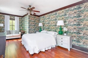 Een slaapkamer met een houten vloer, een bed met wit beddengoed, een nachtkastje met een groene lamp en een plafondventilator.