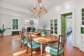 Een eetkamer met een houten tafel, groene bekleden stoelen en een kroonluchter.