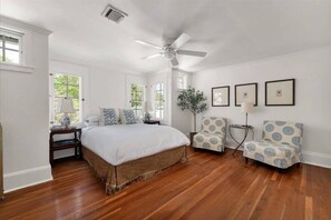 Un dormitorio con una cama grande, una silla, una lámpara de pie y cuadros enmarcados en la pared.