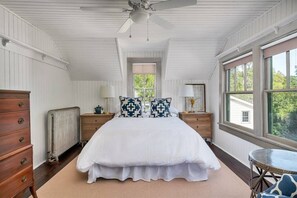 Un dormitorio con una cama grande, mesitas de noche de madera, un aparador, un radiador y una ventana con vistas a la vegetación.
