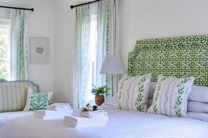 Un lit bien fait, avec des serviettes pliées, une lampe de chevet et une tête de lit à motifs verts.