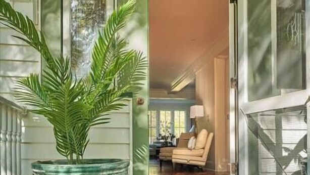 A wooden porch with a large potted plant, a door leading to an interior room with a chair and a table, and a glass door on the right. - ★ LUXURY 5 BR VILLA Heart of Village Steps From #2 (Pinehurst)
