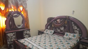 Een slaapkamer met een bloemenprint bedspreider, een decoratief hoofdbord, een nachtkastje en een bijzettafeltje.