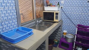 Een kleine keuken met een magnetron, spoelbak en een blauwe afwasslede.