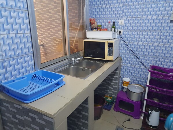 A compact kitchen with a microwave, sink, and a blue dish rack. - Diallo Guest House 1 (Conakry)
