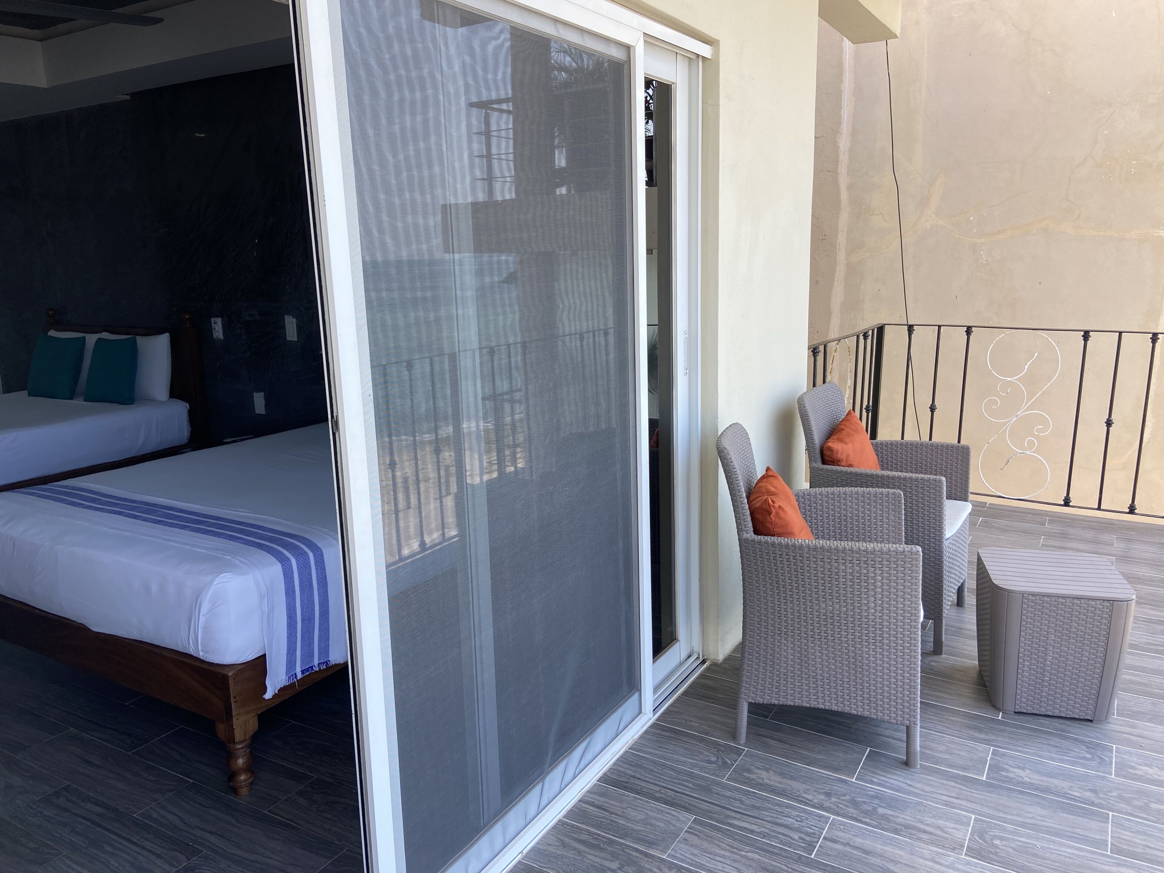 Ein Hotelzimmer mit einem Bett, einer Glasschiebetür, die auf einen Balkon führt, und Korbmöbeln.