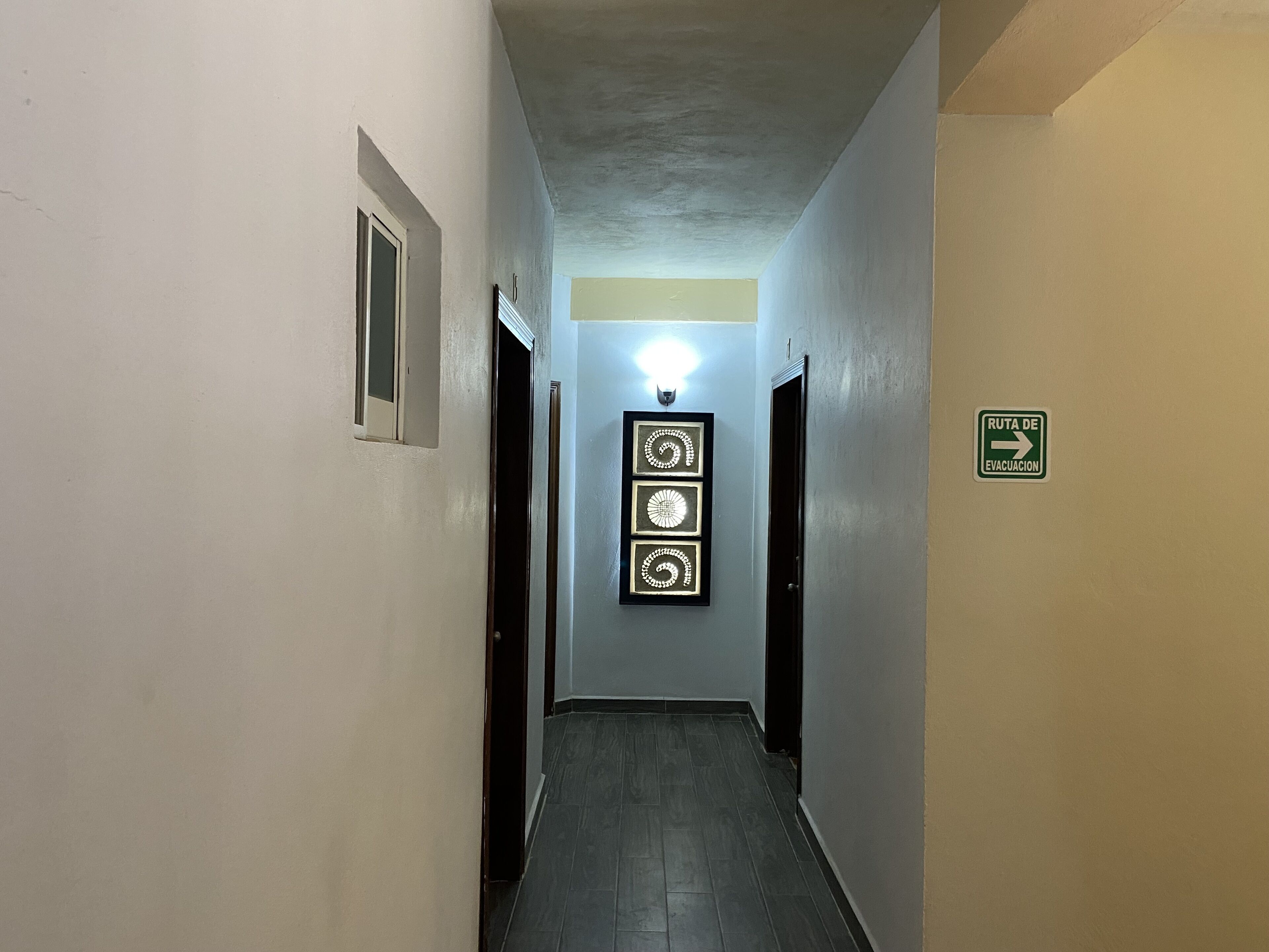Un corridoio stretto con un lampadario, una porta con un segnale che indica la via di fuga e opere d'arte appese al muro.