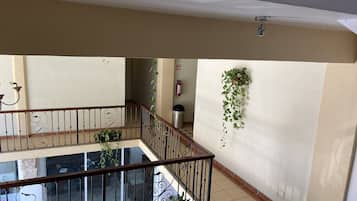Un interior de varios niveles con un balcón, plantas en macetas y un extintor.