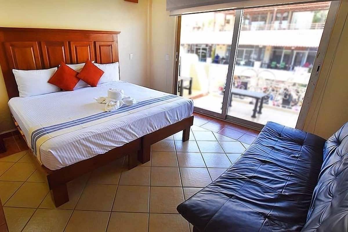 Une chambre d’hôtel avec un lit, une tête de lit en bois, un canapé bleu et une vue sur l’extérieur.