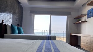 Een slaapkamer met een groot bed, uitzicht op het strand en een houten dressoir.