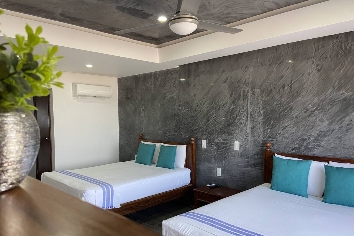 Une chambre d’hôtel avec deux lits, un ventilateur de plafond et une plante sur une table.