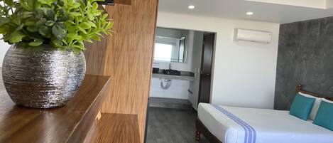Habitación de hotel moderna con una cama de madera, una planta en maceta y vistas al baño.