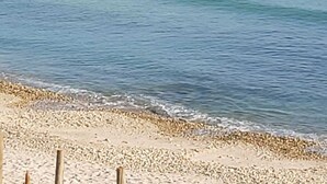 Een strand met helderblauw water, een rotsachtige kustlijn en enkele boten in de verte.