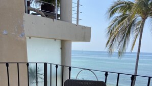 Een balkon met rieten meubilair, uitzicht op het strand en een palmpboom.