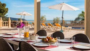 Un área de comedor al aire libre con mesas preparadas para dos, sombrillas y vistas al mar.