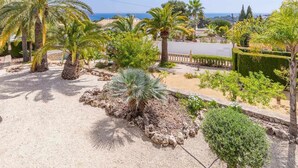 Un jardín con palmeras, setos y vista al mar.