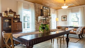 Un comedor con una larga mesa de madera, sillas, una pared de acento de piedra y una zona de estar acogedora con cojines.
