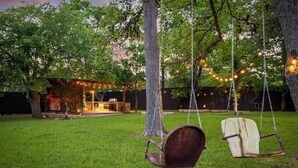 Un patio trasero con un parque infantil, un banco de madera y luces colgantes.