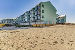 Un hôtel à plusieurs étages, doté de balcons, situé sur une plage de sable.