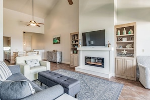 A spacious living room with a fireplace, a television, and a bookshelf. - Waterfront Condo on Pensacola Beach (Pensacola Beach)