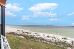 Une vue sur la plage depuis un balcon, avec une clôture en bois et une zone herbeuse au premier plan.