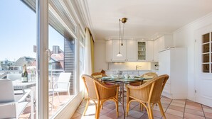 Una cocina moderna con armarios blancos, una mesa de comedor con sillas de mimbre y un ventanal con vistas a un paisaje urbano.